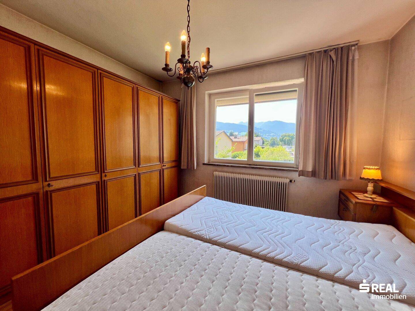 Schlafzimmer mit Doppelbett, Holzschrank und Fenster mit Bergblick.