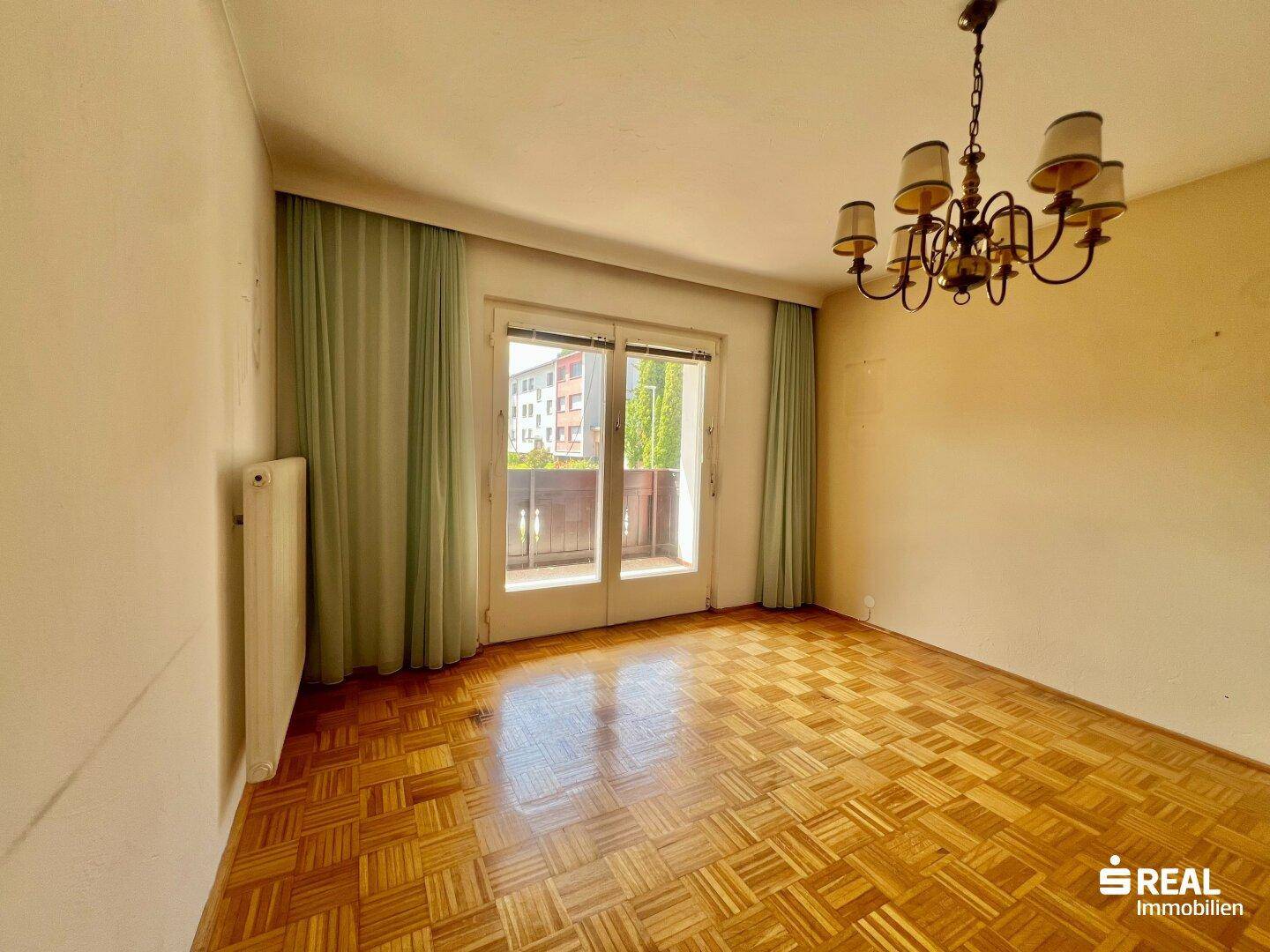Leeres Schlafzimmer mit Parkettboden und Zugang zum Balkon.