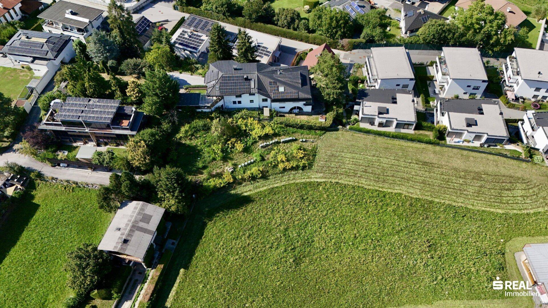 Panoramablick aus der Vogelperspektive auf Wohnhäuser, grüne Felder und die umliegende Berglandschaft.
