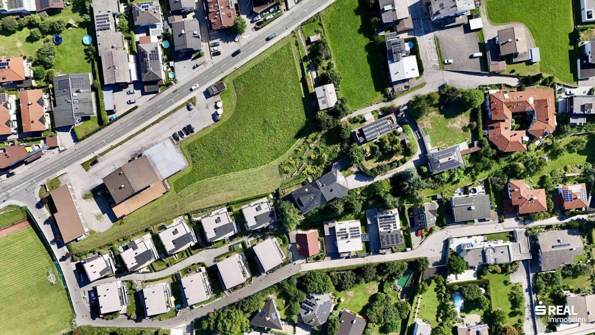 Weitläufige Luftaufnahme einer Siedlung mit Straßen, Wohnhäusern und ausgedehnten Grünflächen.