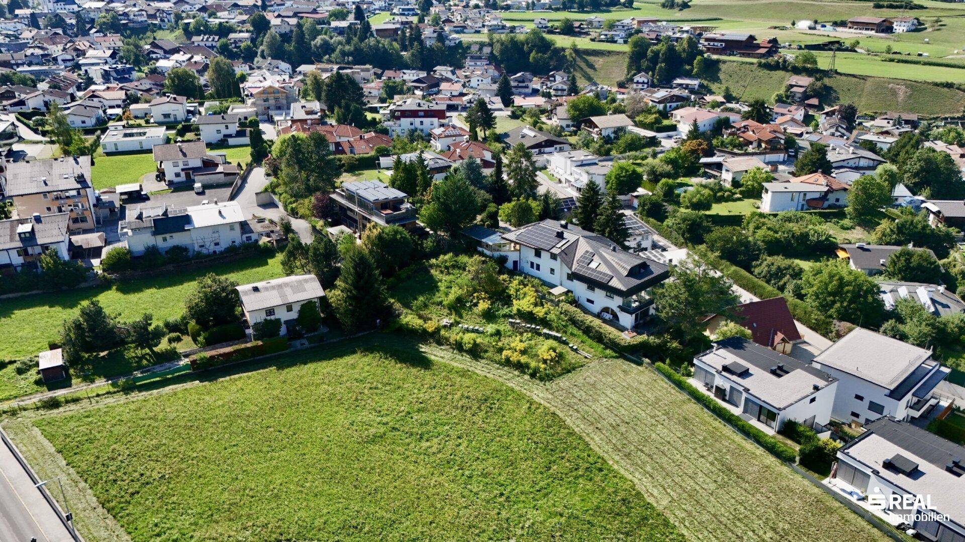 Weitwinkel-Luftaufnahme einer Wohnsiedlung mit angrenzenden Feldern und einer weiten Landschaft.