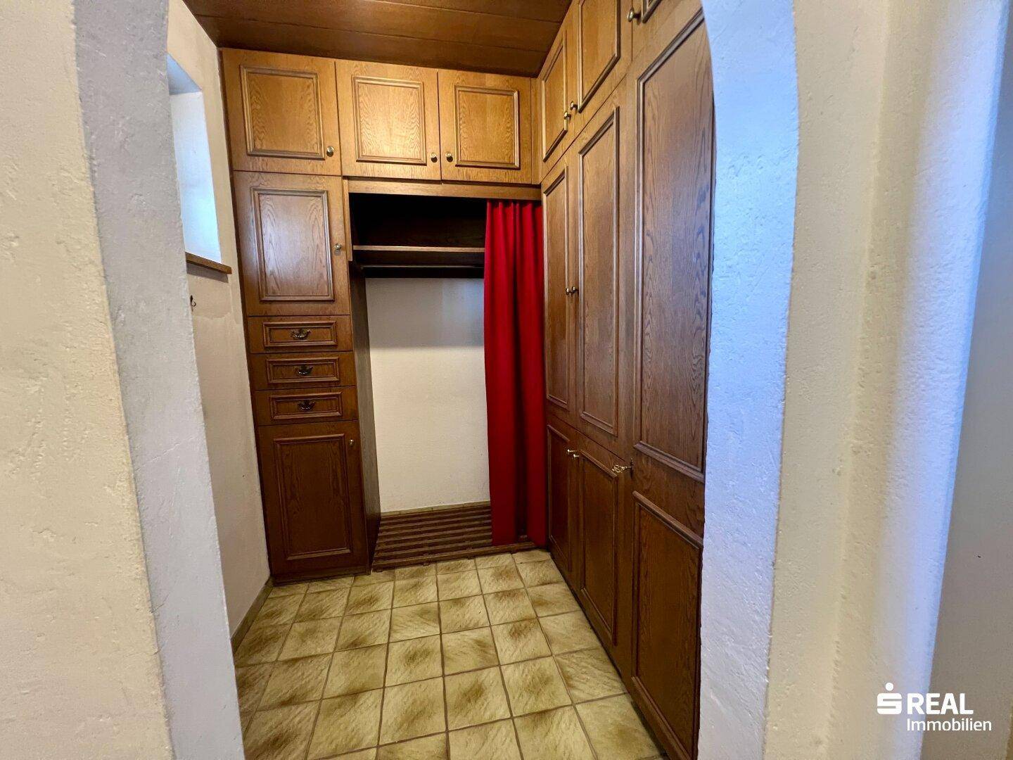 Kleiner begehbarer Schrankbereich mit Holzschränken und gefliestem Boden.