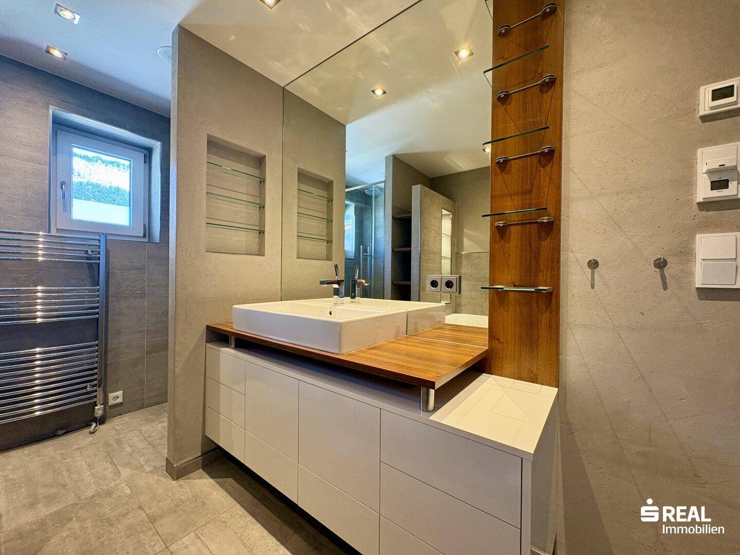 Detailansicht des modernen Badezimmers mit Einzelwaschbecken, großem Spiegel und Holzablage, mit Fenster.