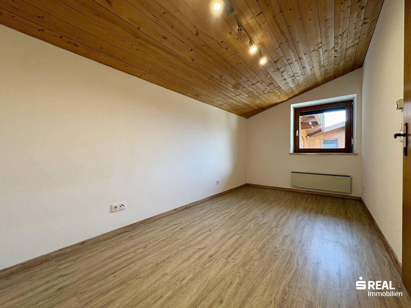 Gemütliches Zimmer mit schräger Holzdecke, Laminatboden und einem Fenster, ideal als Schlafzimmer.