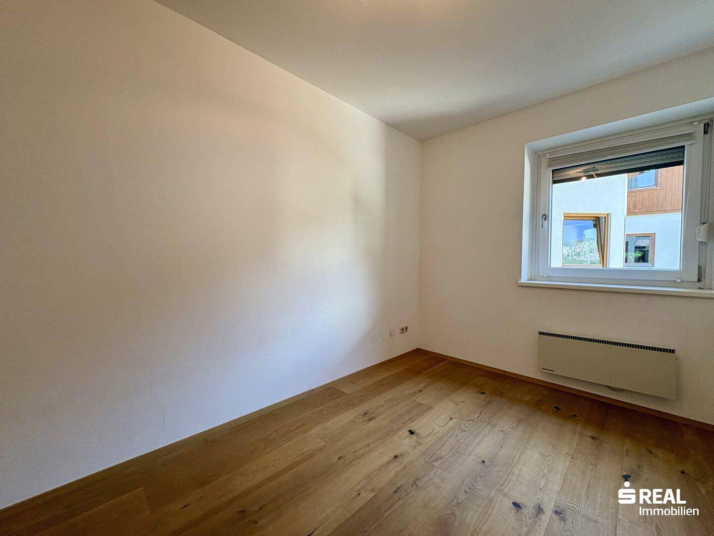 Schlichtes Zimmer mit weiß gestrichenen Wänden, Holzboden und einem Fenster, bereit zur individuellen Gestaltung.