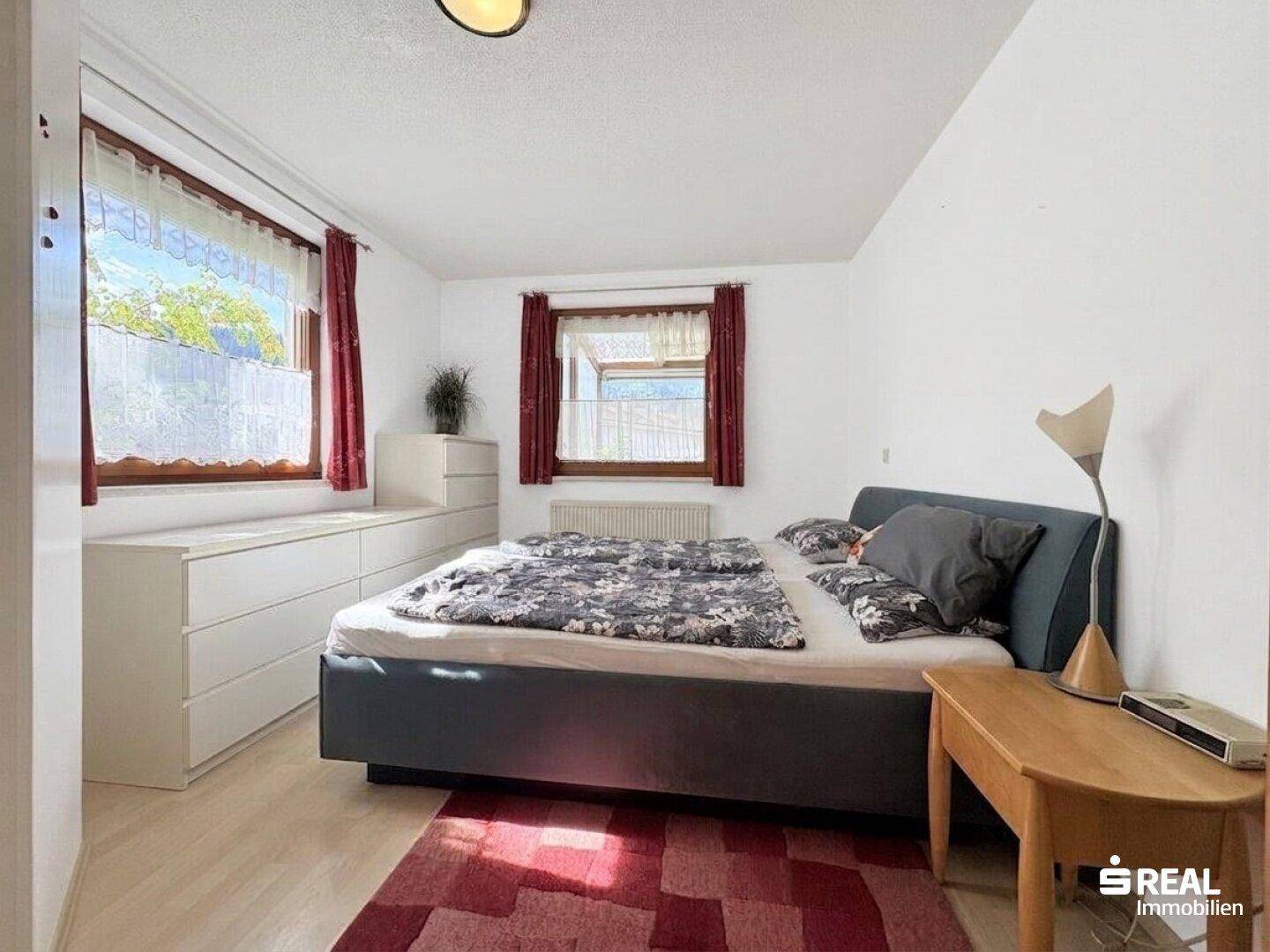 Gemütliches Schlafzimmer mit Doppelbett, weißen Kommoden und hellem Holzboden, mit zwei Fenstern.