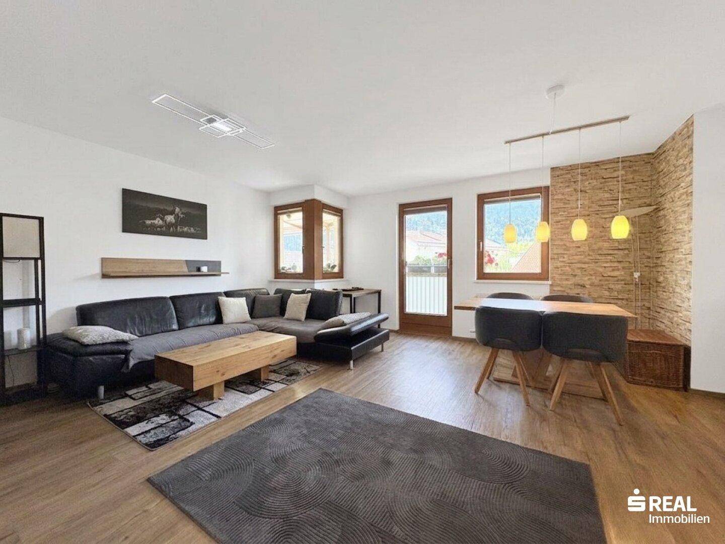 Geräumiger Wohnbereich mit großem Sofa, Esstisch und dekorativer Steinwand, hell und einladend.