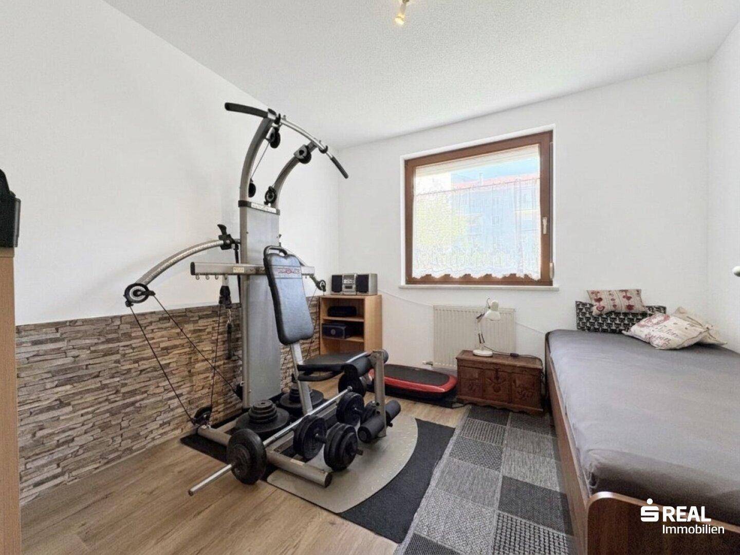 Schlafzimmer mit Fitnessgerät und Einzelbett, ideal für Sportbegeisterte, mit Holzboden.