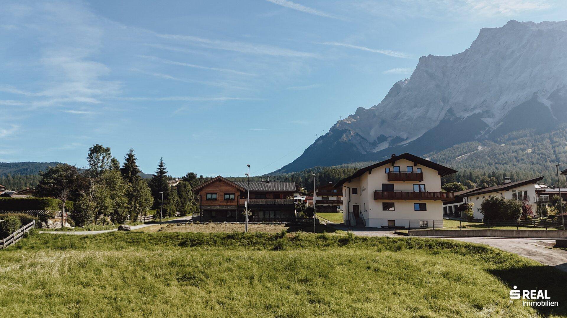 Großes grünes Grundstück mit Blick auf traditionelle Häuser und eine imposante Bergkulisse.