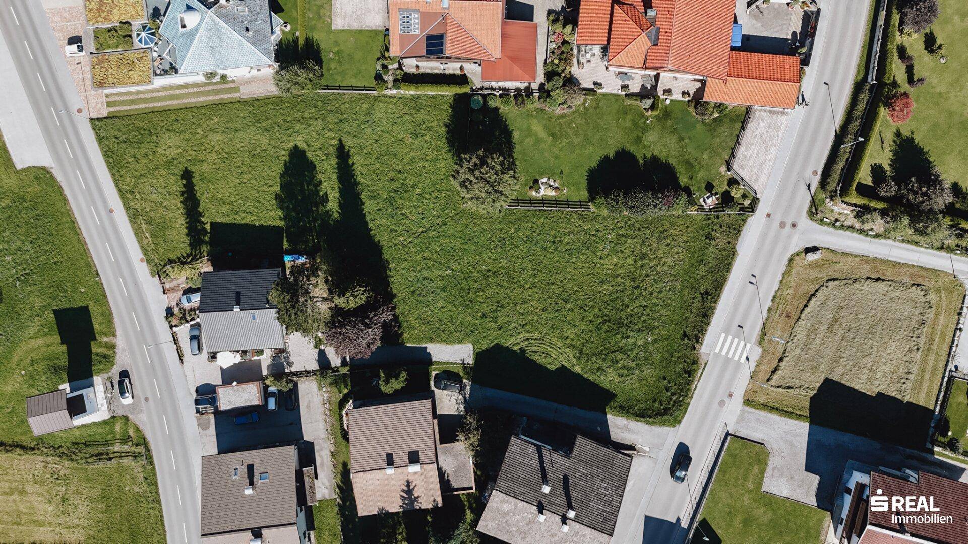 Weitläufiges grünes Grundstück an einer Kreuzung, umgeben von Wohngebäuden und Straßen.