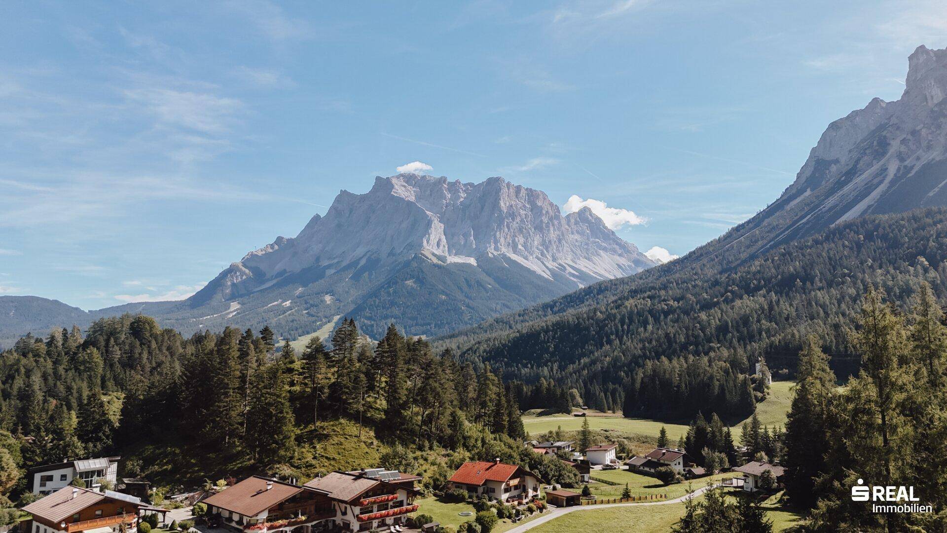 Panoramablick auf ein Dorf in einem Tal, umgeben von dichten Wäldern und majestätischen Bergen.
