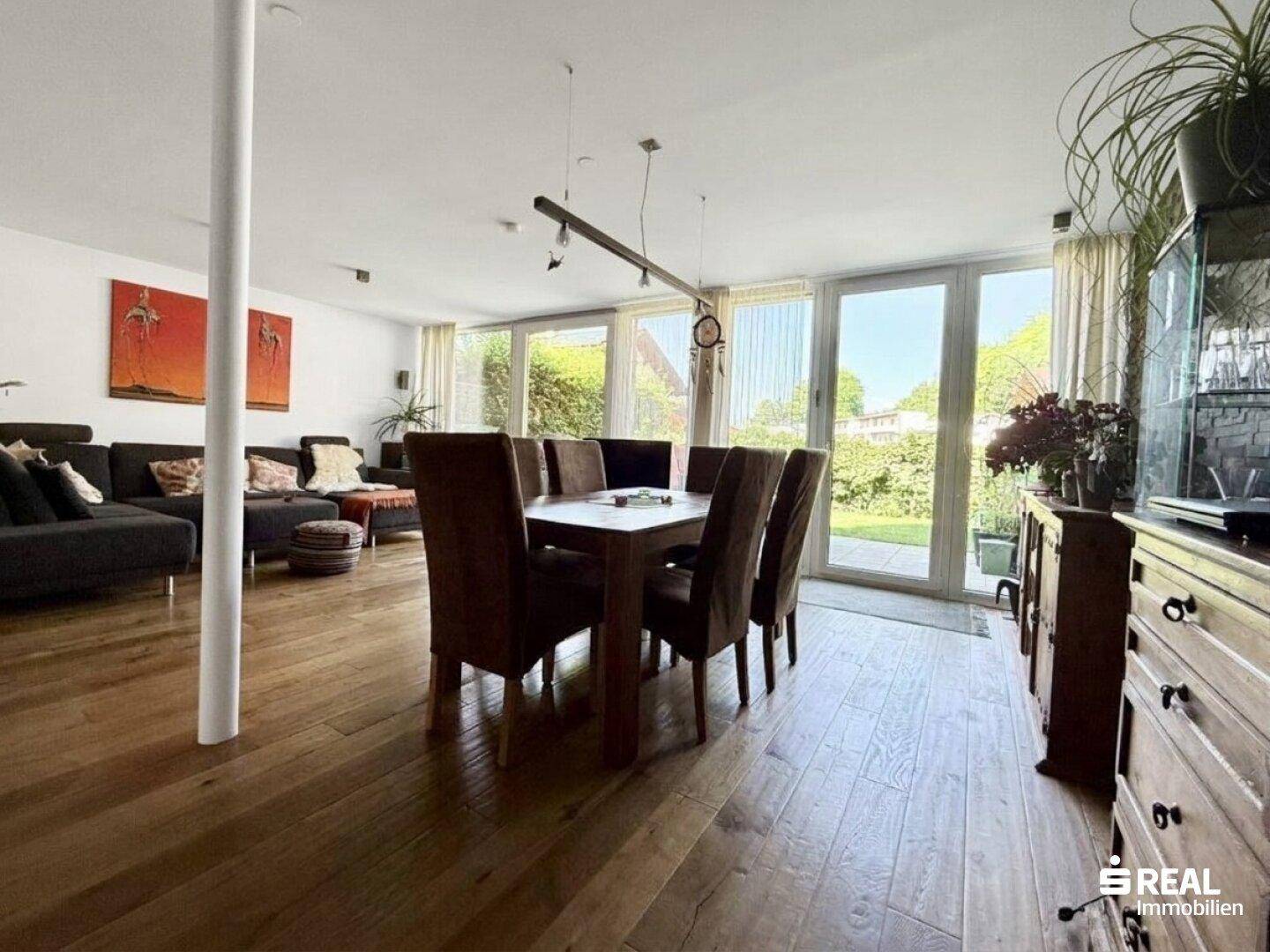 Geräumiger Wohn-Essbereich mit Holzboden, großem Esstisch und Zugang zum Garten.