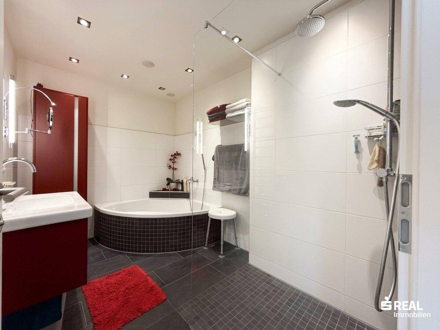 Modernes Badezimmer mit Eckbadewanne, ebenerdiger Dusche und dunklen Bodenfliesen.