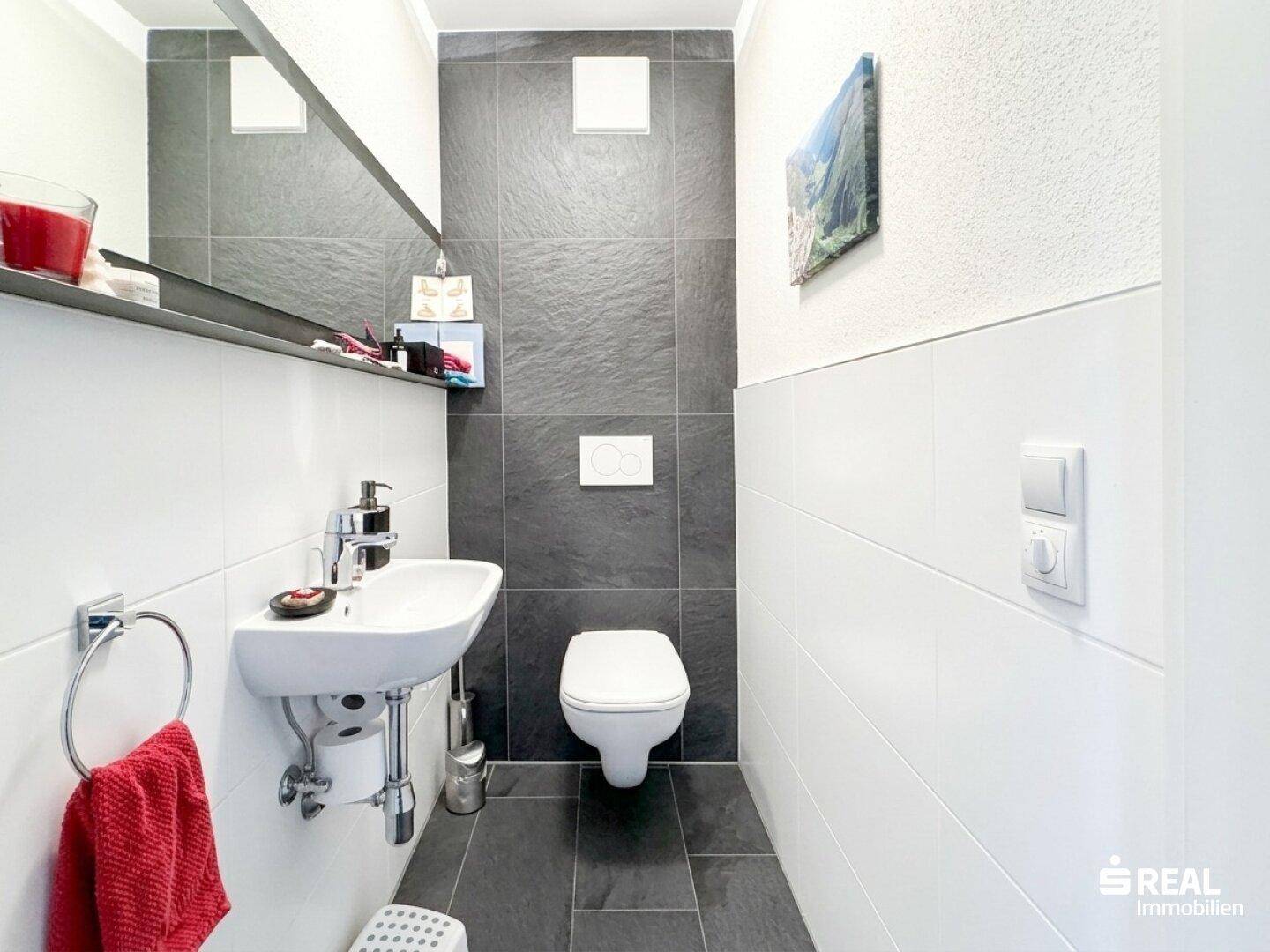 Modernes Gäste-WC mit Wand-WC, kleinem Waschbecken und dunklen Fliesen.