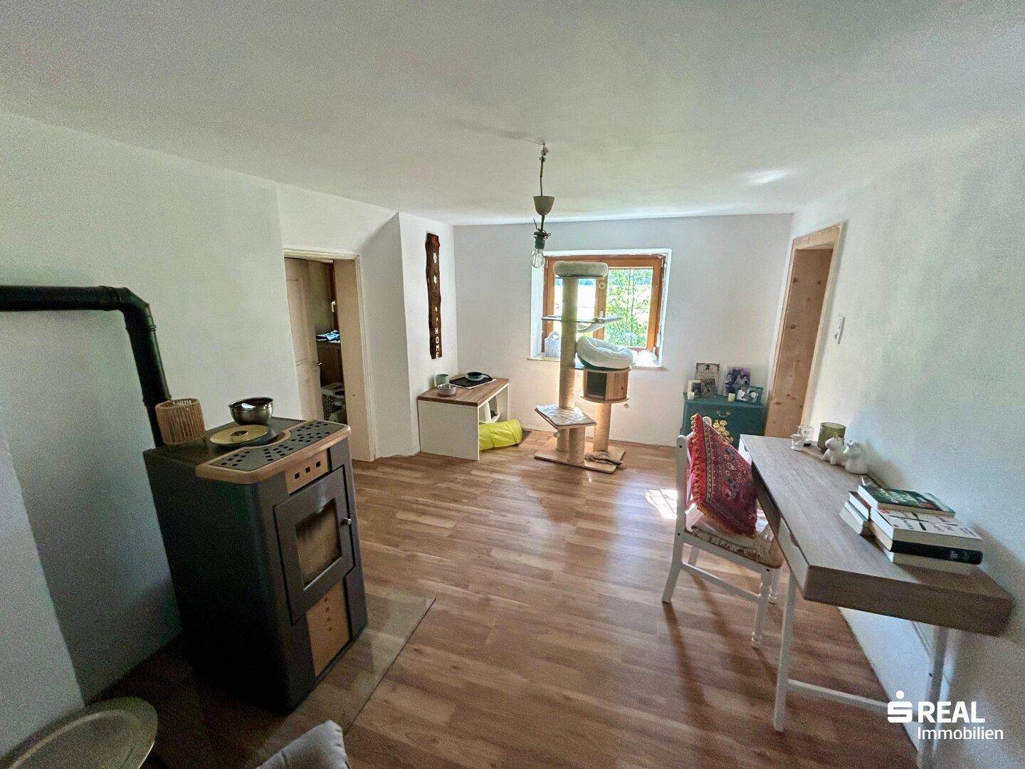 Helles Arbeitszimmer mit Holzofen, Schreibtisch und Blick ins Grüne.