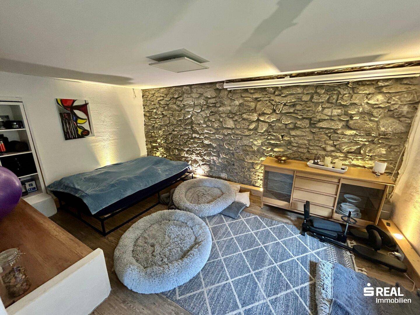 Schlafbereich mit rustikaler Steinwand, bequemer Liegefläche und Teppichboden.