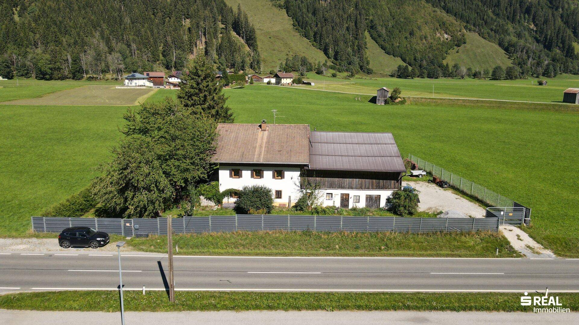Das Haus in ländlicher Umgebung mit Blick auf die bewaldeten Berghänge und weite Wiesen.