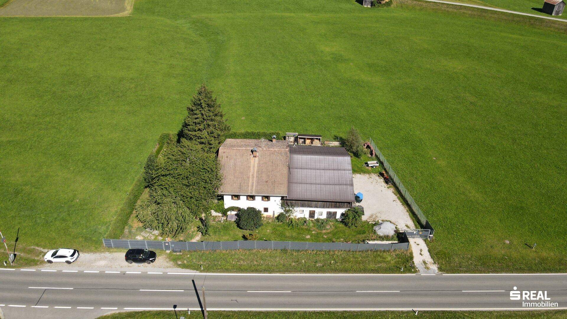 Weitläufige Luftaufnahme des Anwesens mit angrenzender Straße und weitläufigen grünen Feldern.