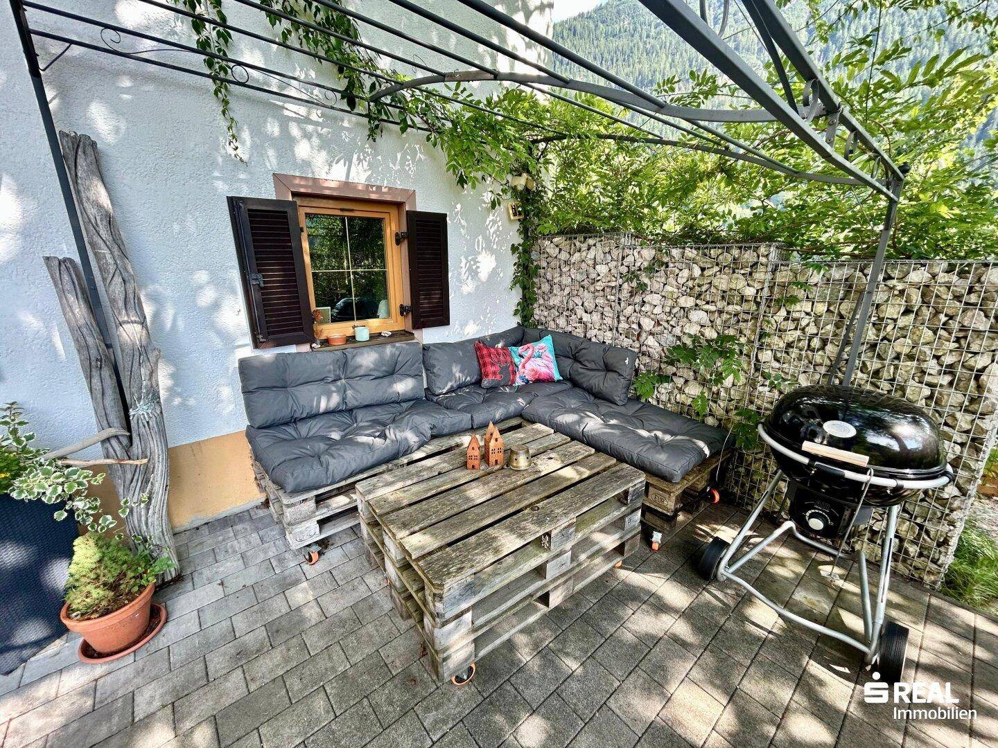 Detailansicht der Terrasse mit bequemen Palettenmöbeln, Grill und Gabionenwand.