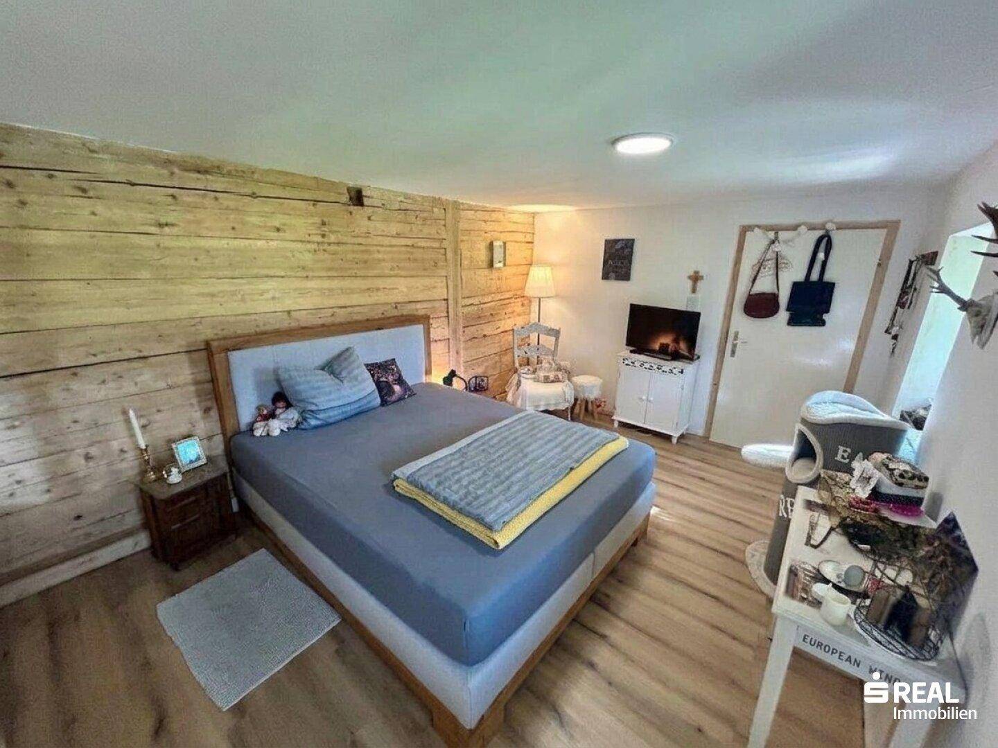 Gemütliches Schlafzimmer mit Holzwandverkleidung, Doppelbett und rustikalen Dekorationselementen.