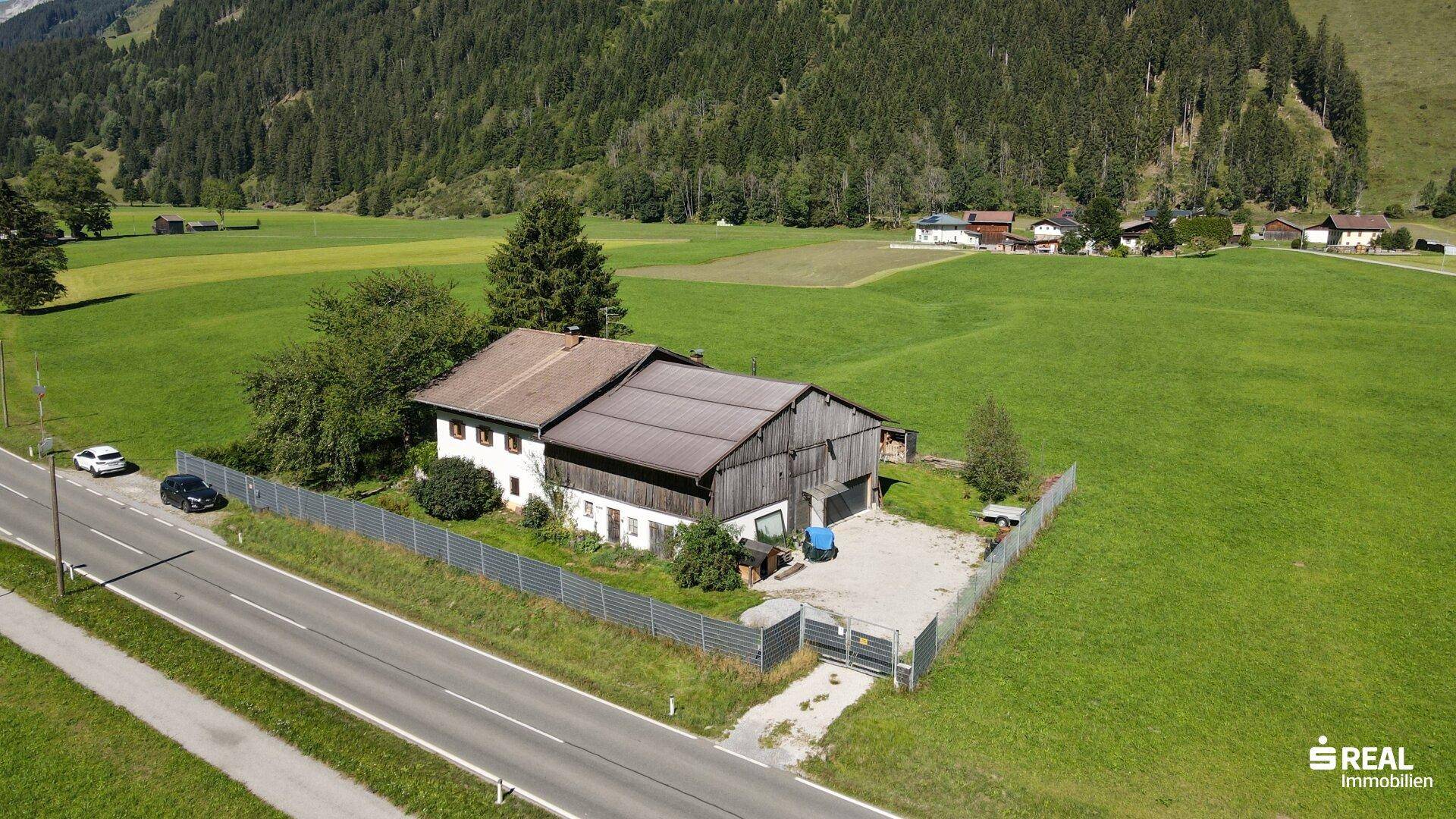 Seitenansicht des Hauses mit angrenzendem Schuppen und großem Kiesbereich neben der Straße.