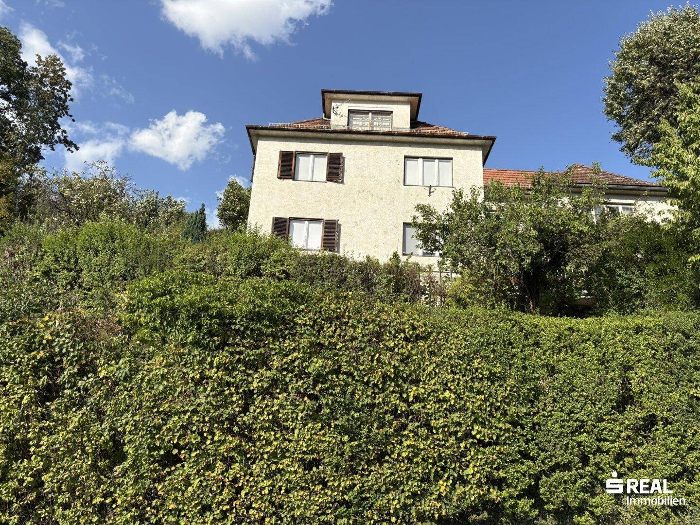 Ein traditionelles Haus mit Satteldach, teilweise verdeckt von einer hohen, gepflegten Hecke.