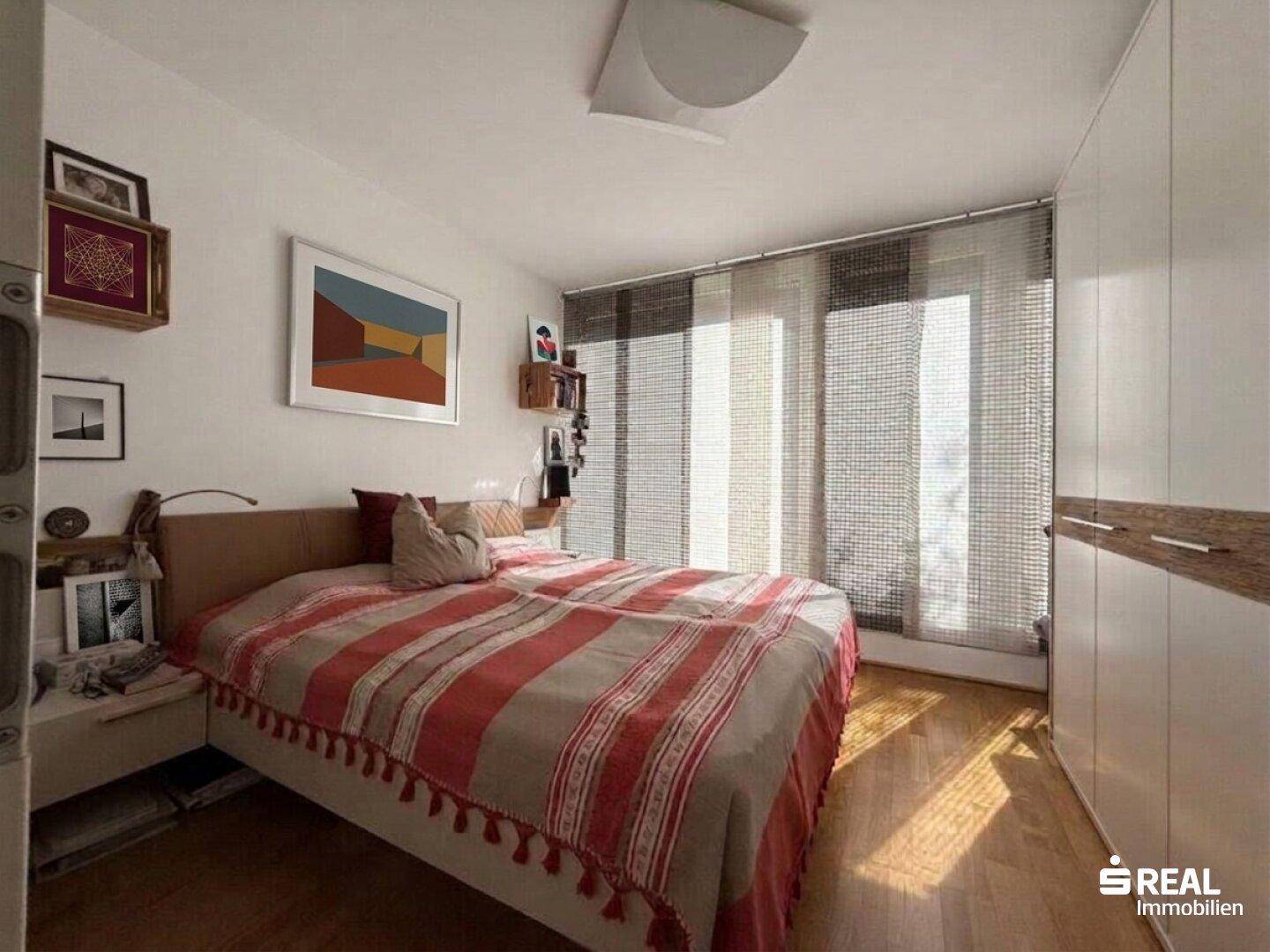 Gemütliches Schlafzimmer mit Holzboden, großem Bett und Einbauschrank, bietet direkten Zugang zum Balkon.
