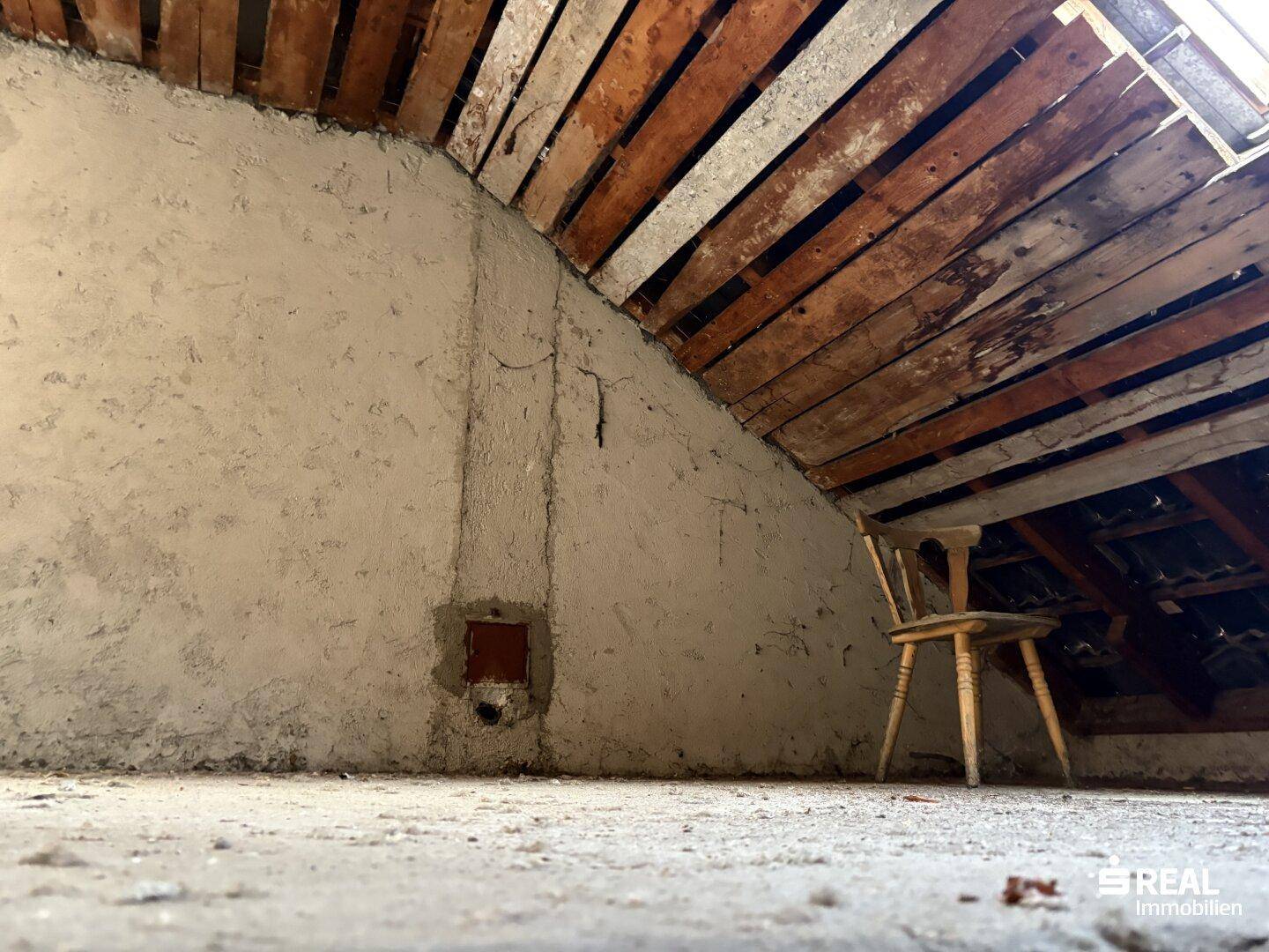 Unfertiger Dachbodenbereich mit freiliegenden Holzbalken und einer schlichten Holzstuhl, der das Potenzial zeigt.