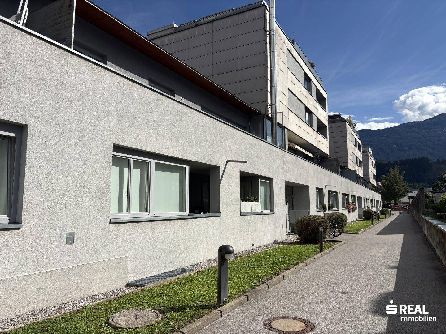 Moderne Wohnanlage mit grauer Fassade, Balkonen und Blick auf die umliegende Berglandschaft.