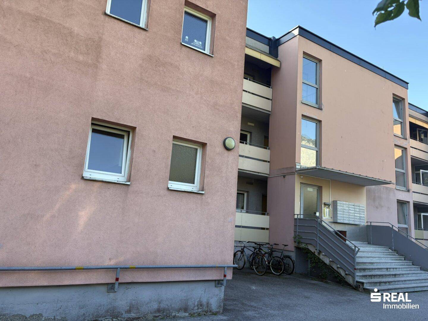 Eingangsbereich des Gebäudes mit Treppe, Briefkästen und abgestellten Fahrrädern.