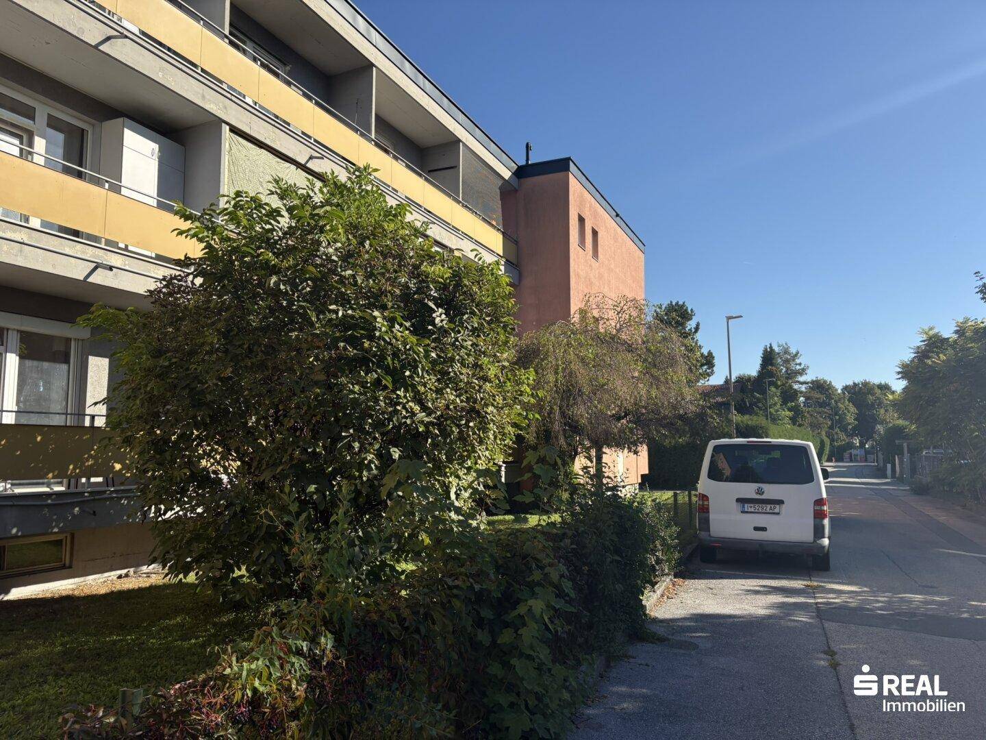 Seitenansicht des Gebäudes von der Straße aus, umgeben von Bäumen und einem geparkten Lieferwagen.