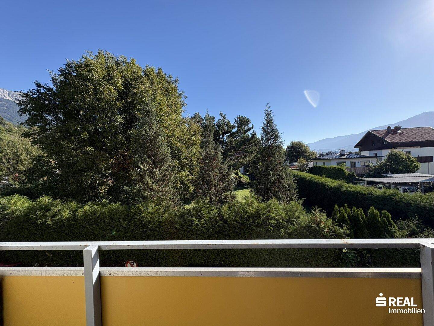 Sonniger Ausblick vom Balkon auf grüne Bäume und die umliegende Wohngegend.