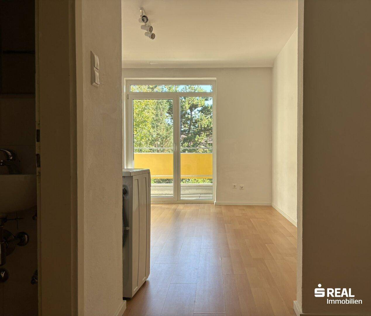 Geräumiges Zimmer mit Holzboden und Balkonzugang, inklusive einer Waschmaschine.