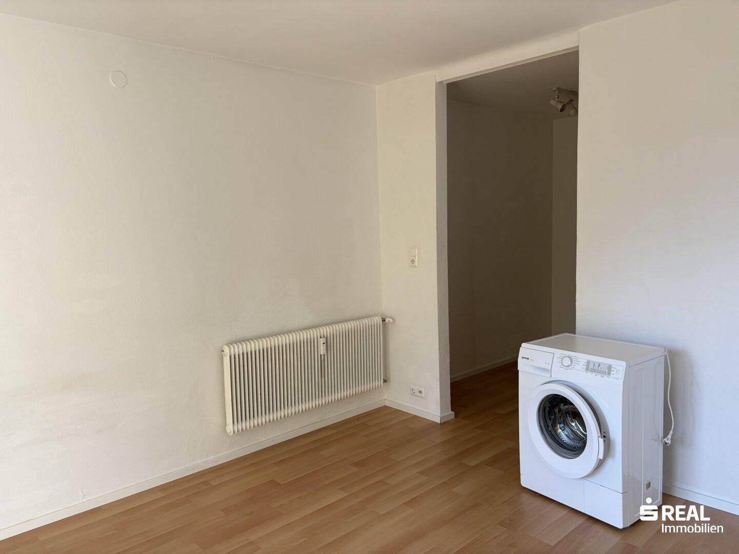 Leerer Raum mit Heizkörper und einer Waschmaschine, ausgestattet mit Holzboden.