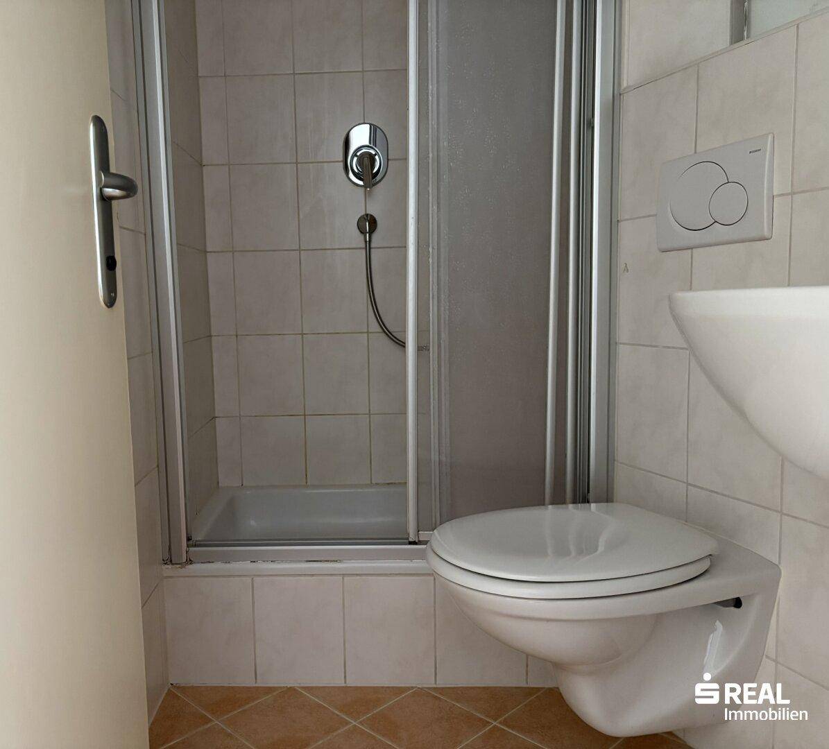 Badezimmer mit Duschkabine, wandhängendem WC und Waschbecken, gefliest in hellen Tönen.