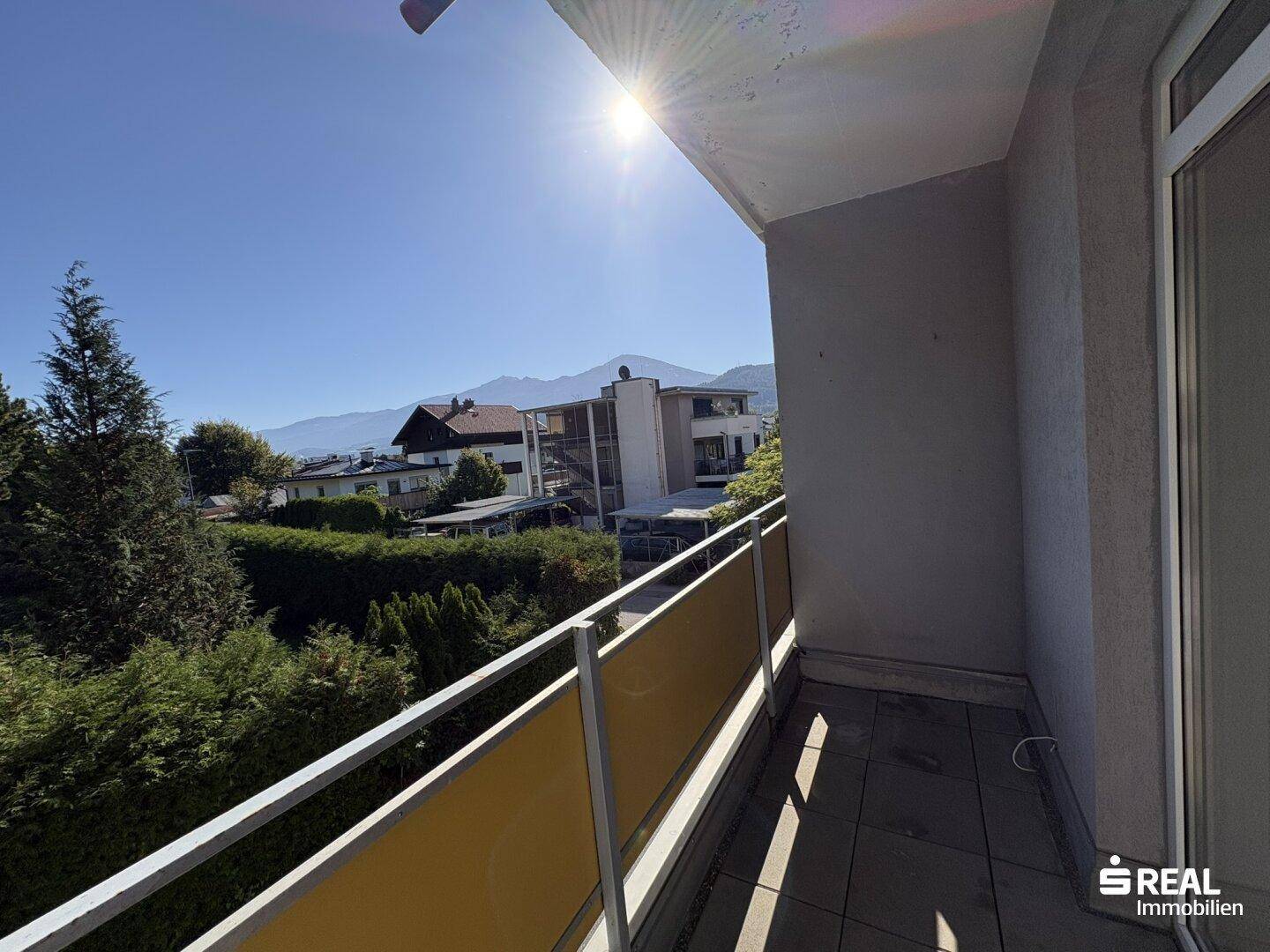 Sonniger Ausblick vom Balkon auf die umliegende Wohngegend mit Bäumen und Bergen.