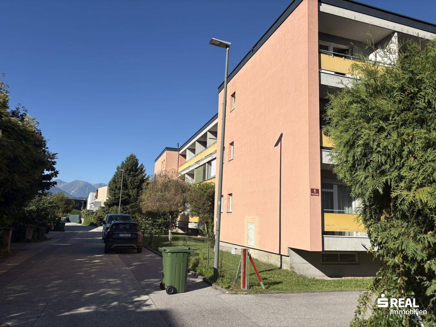 Ruhige Wohnstraße mit geparkten Autos und dem Mehrfamilienhaus im Hintergrund.