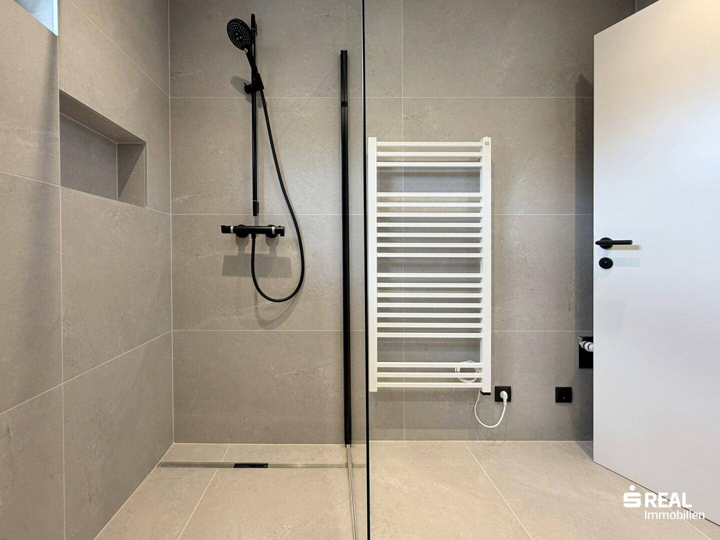 Modernes Badezimmer mit grauen Fliesen, ebenerdiger Dusche und beheiztem Handtuchhalter.