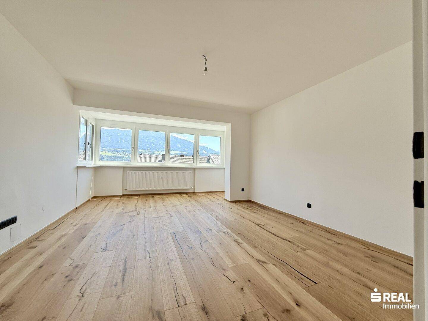 Geräumiges, helles Zimmer mit Holzboden und großen Fenstern, die einen weiten Blick bieten.