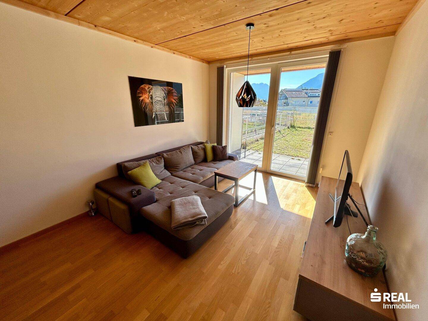 Helles Wohnzimmer mit Holzbalkendecke, Parkettboden und Zugang zur Terrasse.