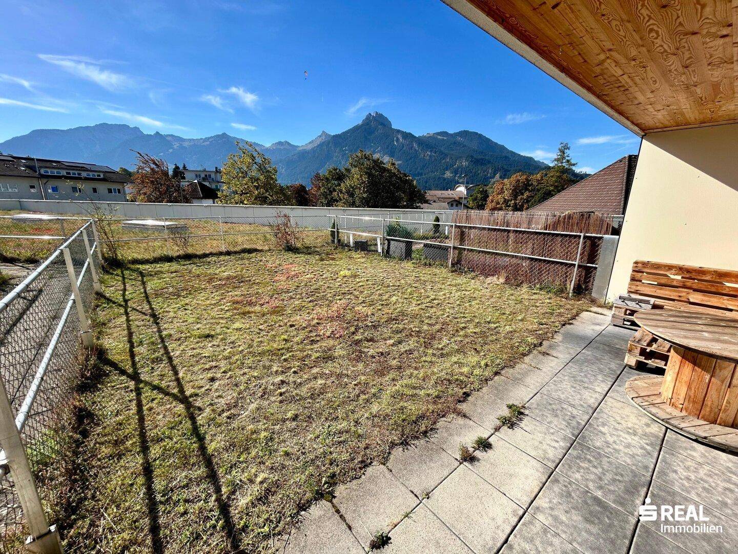 Gartenbereich mit Rasenfläche, Terrasse und beeindruckendem Bergblick.