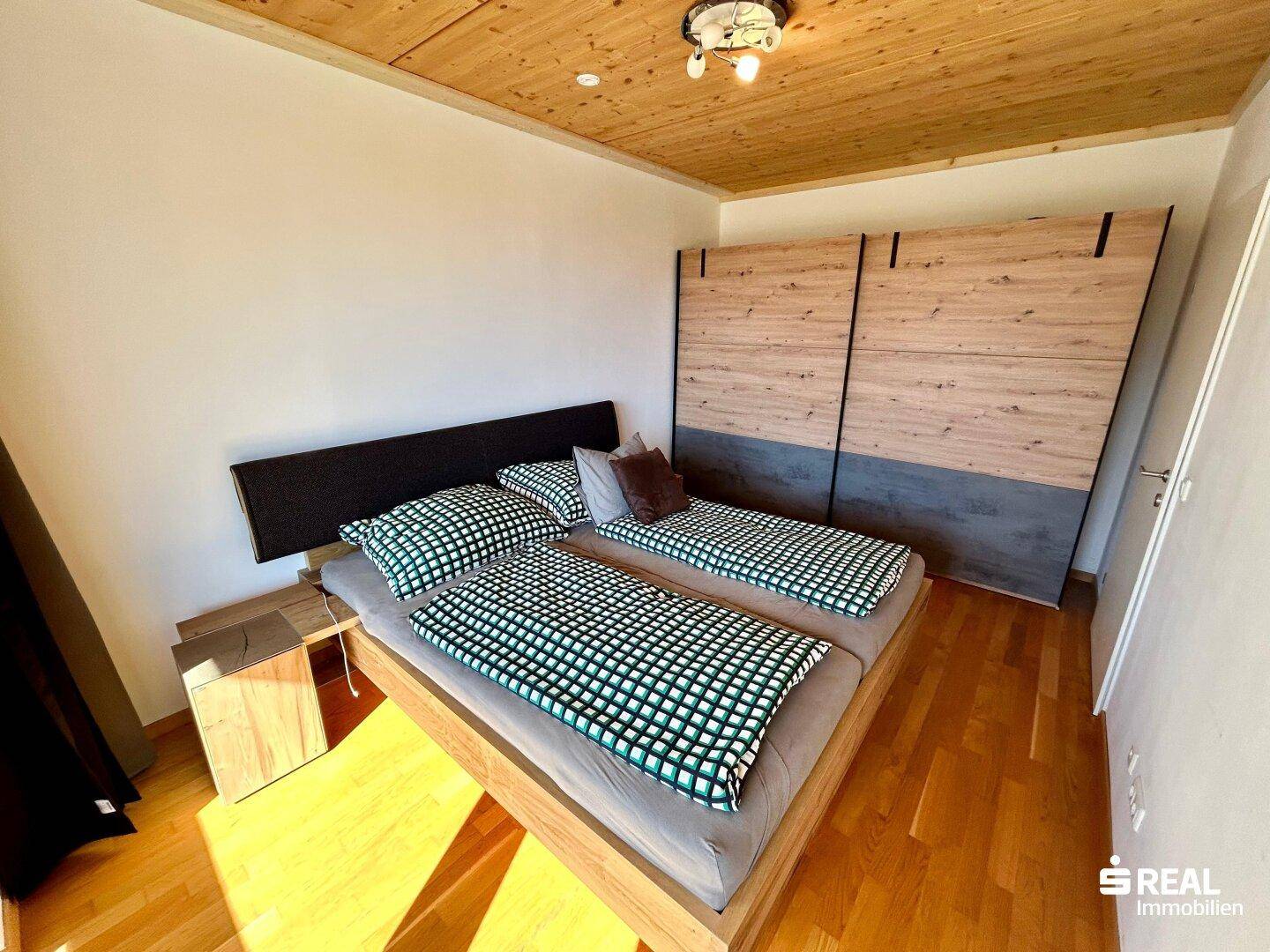 Schlafzimmer mit Holzbalkendecke, Parkettboden und großem Einbauschrank.