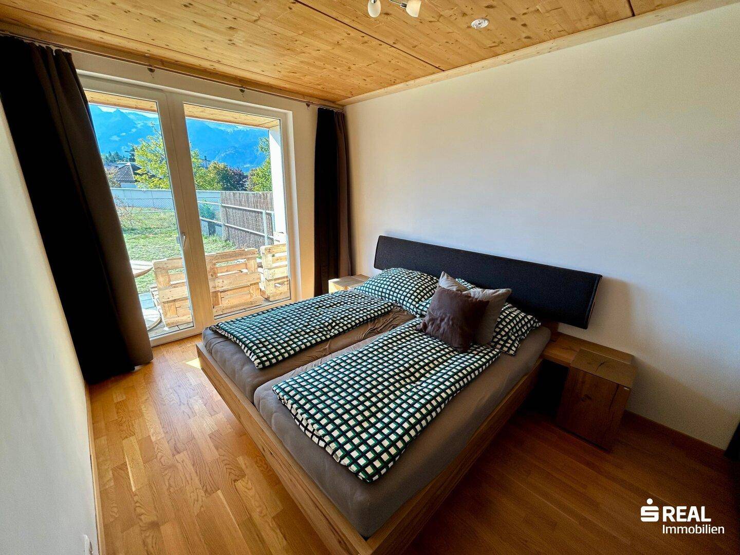 Helles Schlafzimmer mit Holzbalkendecke, Parkettboden und Zugang zum Garten.