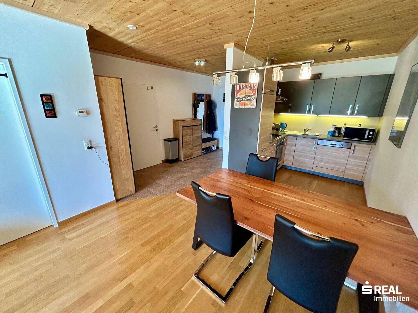 Essbereich mit Holztisch, offener Küche und Zugang zum Eingangsbereich.