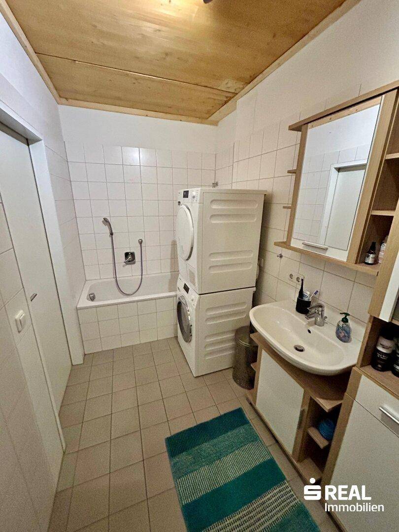 Badezimmer mit Badewanne, Waschmaschine und Trockner, sowie Holzdecke.