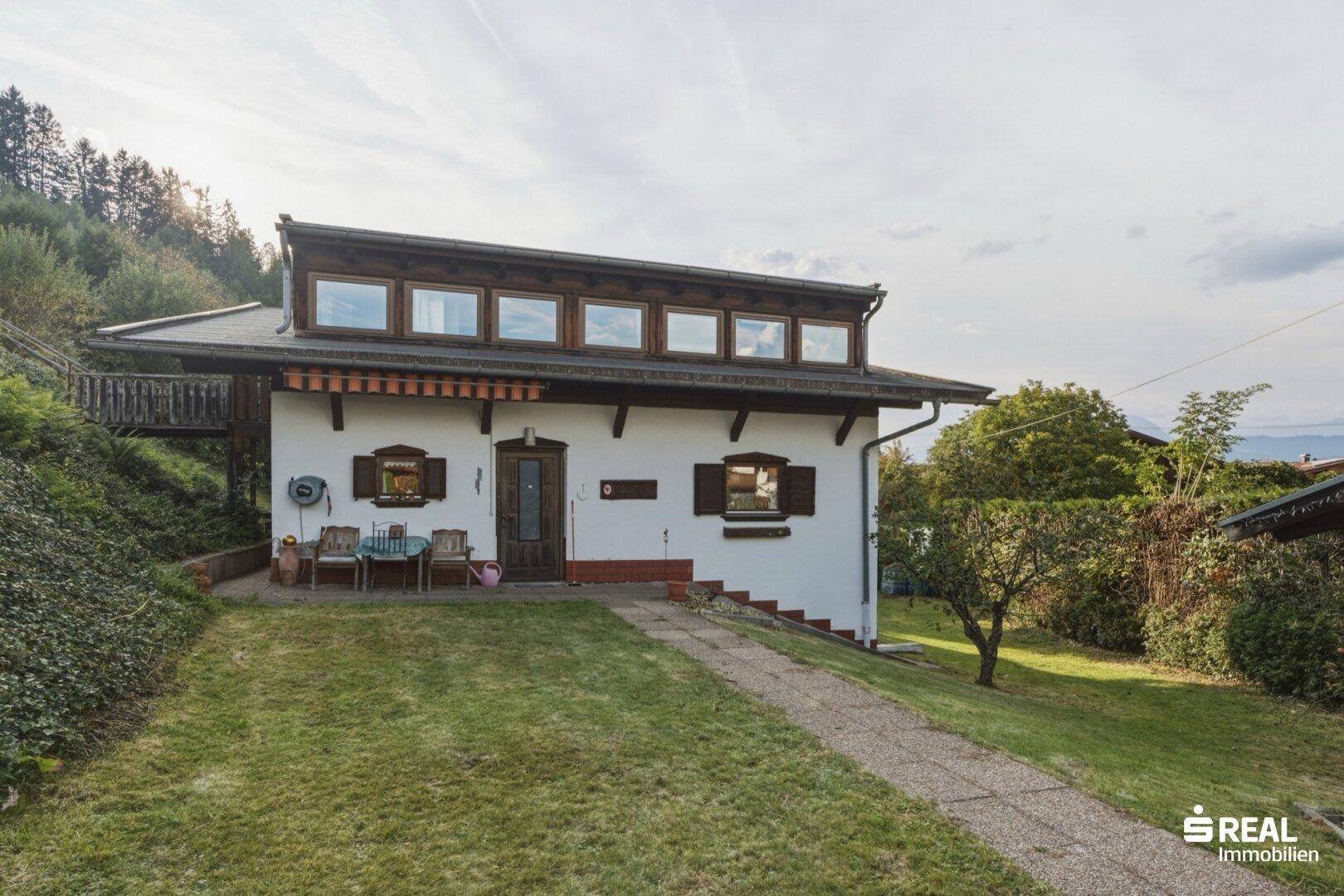 Seitenansicht des Hauses mit kleiner Terrasse und Gartenbereich, umgeben von Natur.