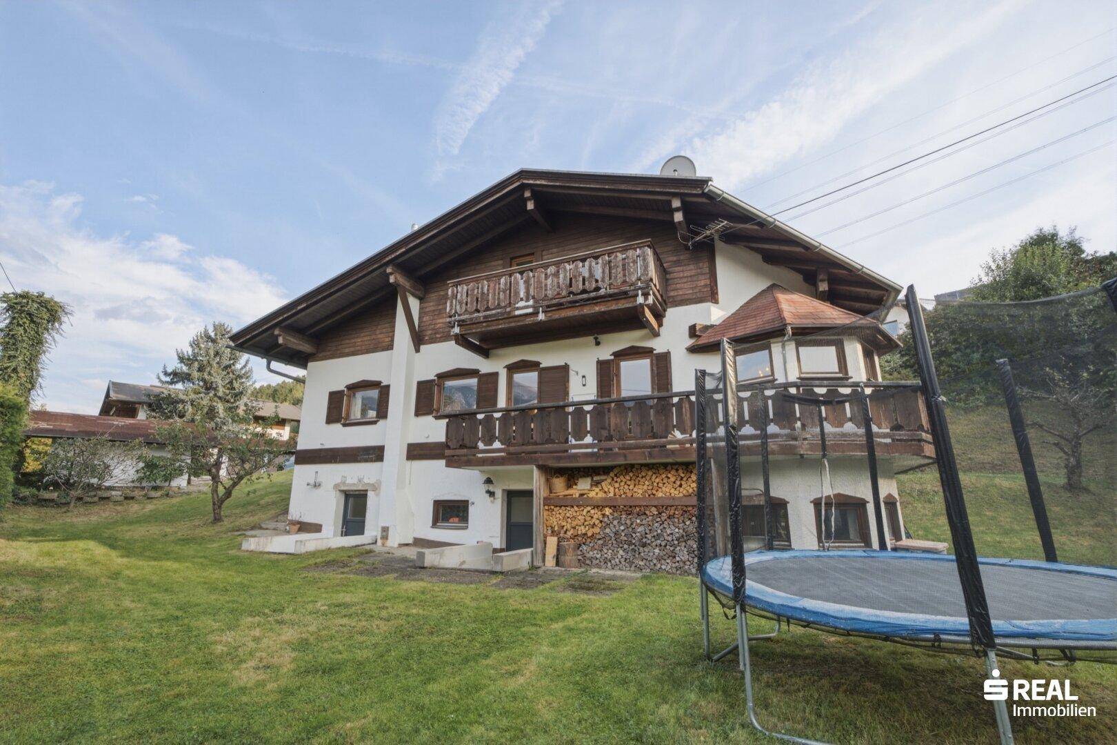 Traditionelles Haus im alpinen Stil mit Holzbalkonen und einem Trampolin im Garten.