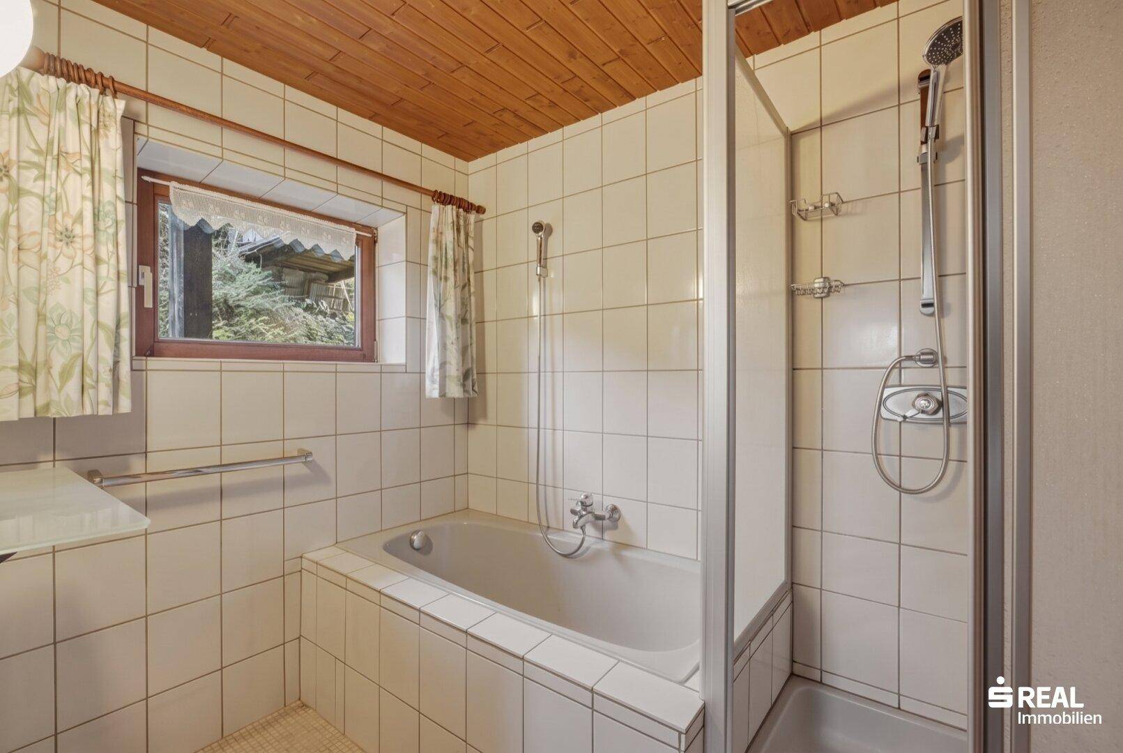 Helles Badezimmer mit Badewanne, Duschkabine und Holzpaneeldecke.