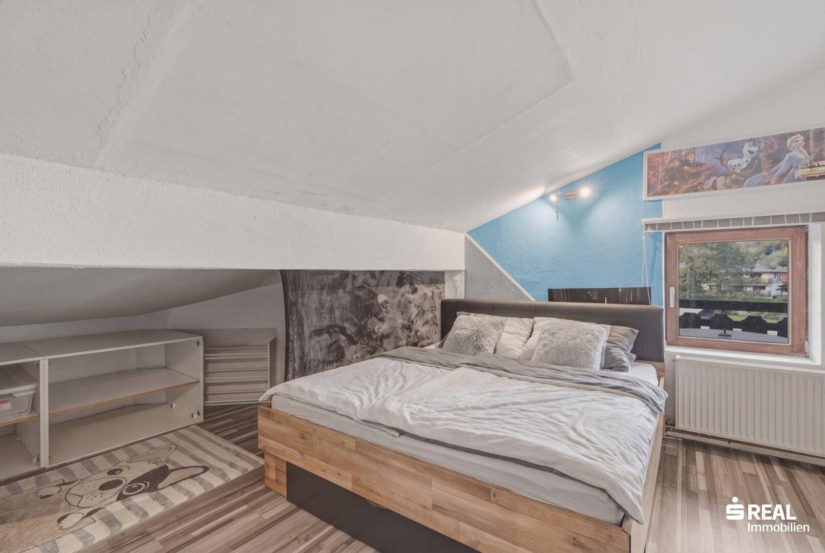 Schlafzimmer im Dachgeschoss mit Holzbett, farbiger Wandgestaltung und Dachschräge.