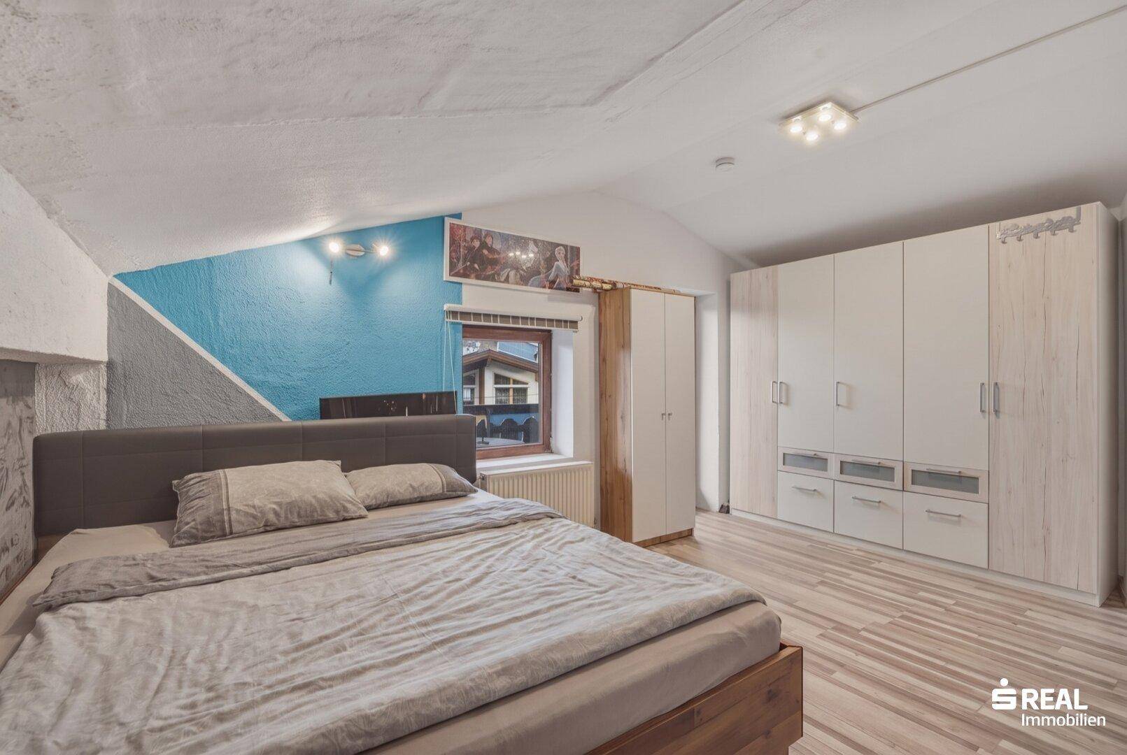 Helles Schlafzimmer im Dachgeschoss mit großem Kleiderschrank und Holzbett.